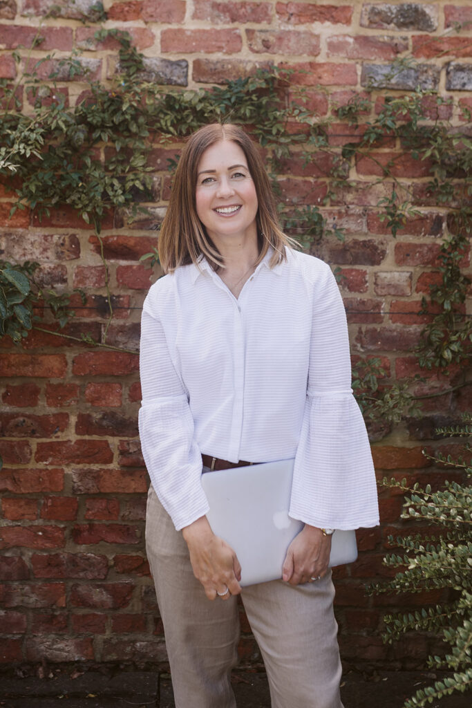 Sally Parker, Marketing Strategist in Yorkshire, stood holding her Macbook in front of a brick wall.